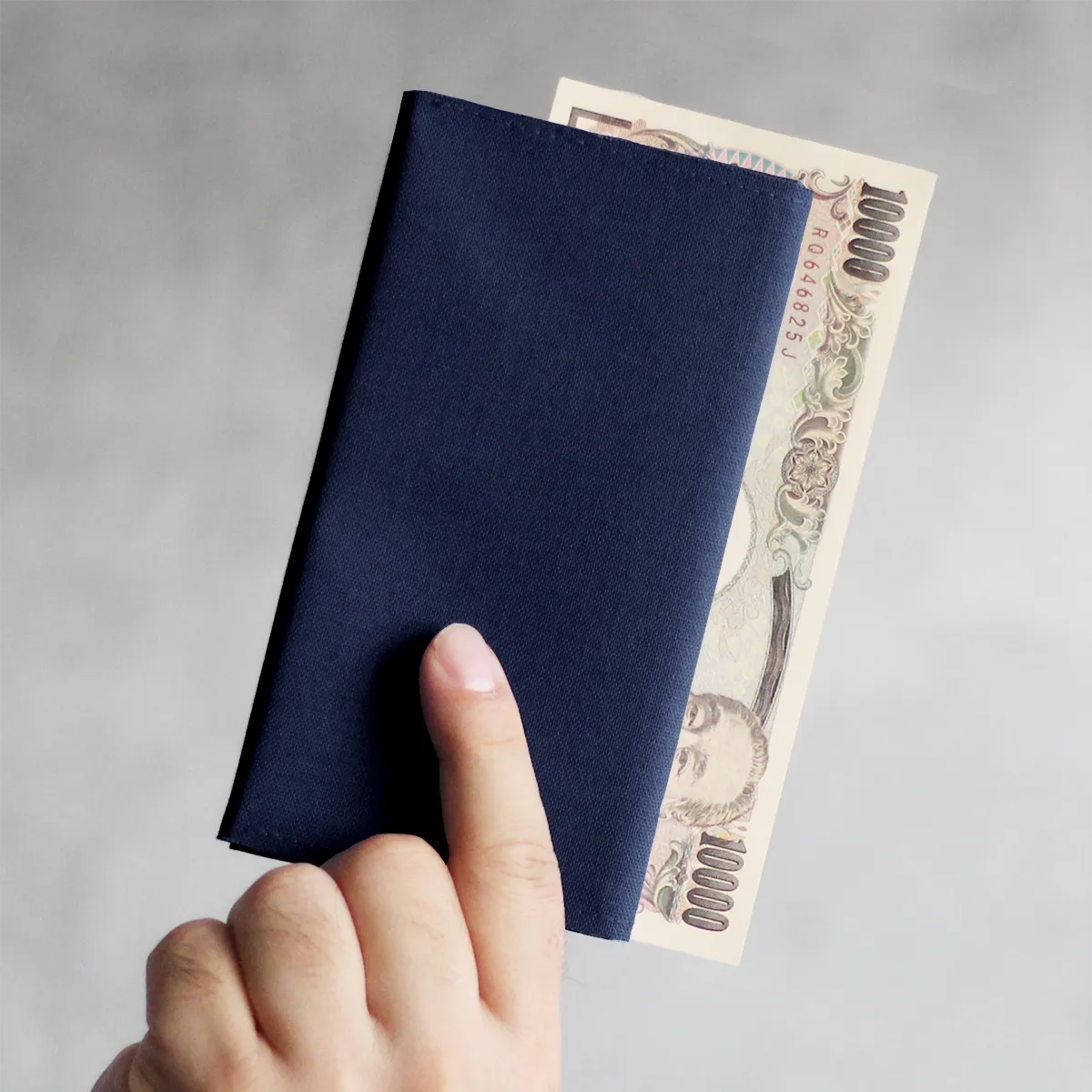 紺色のTyla長財布と一万円札を持っている手