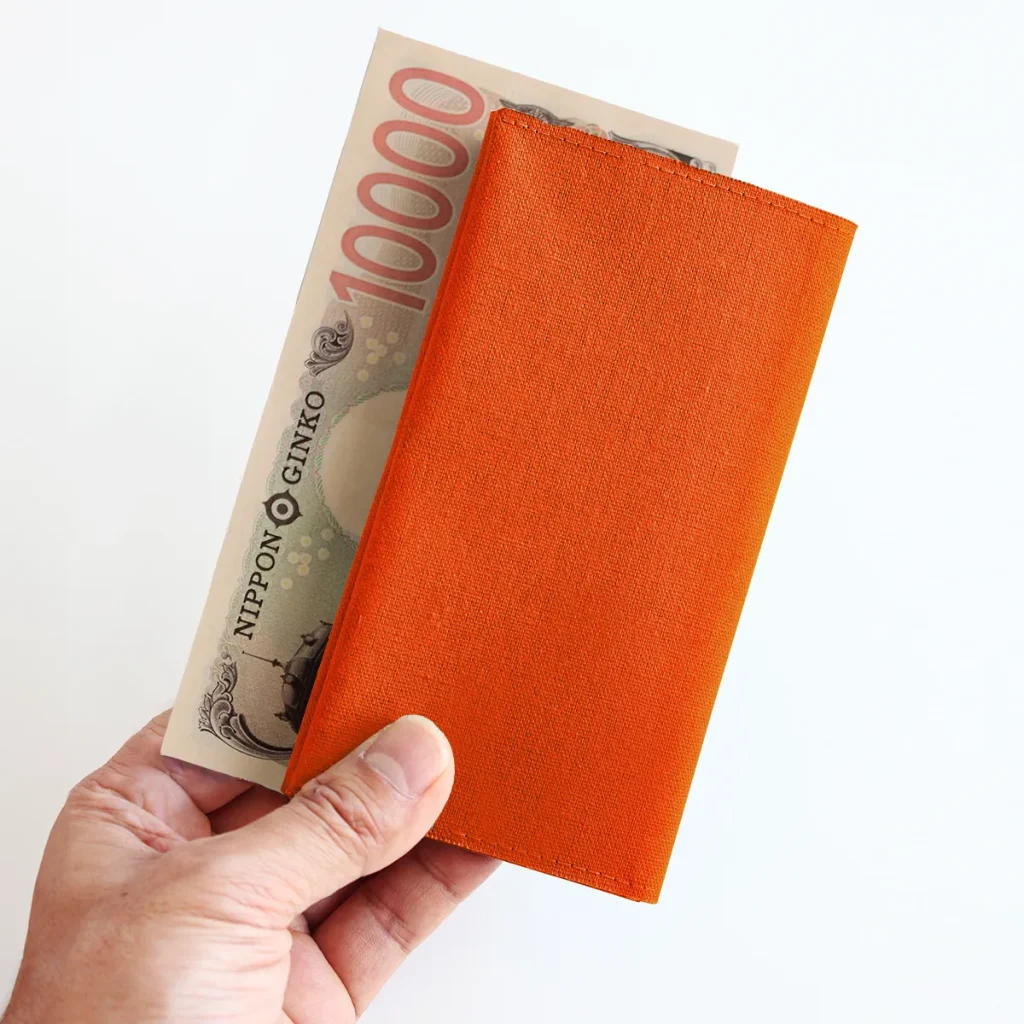Tyla長財布オレンジと一万円札を持っている手