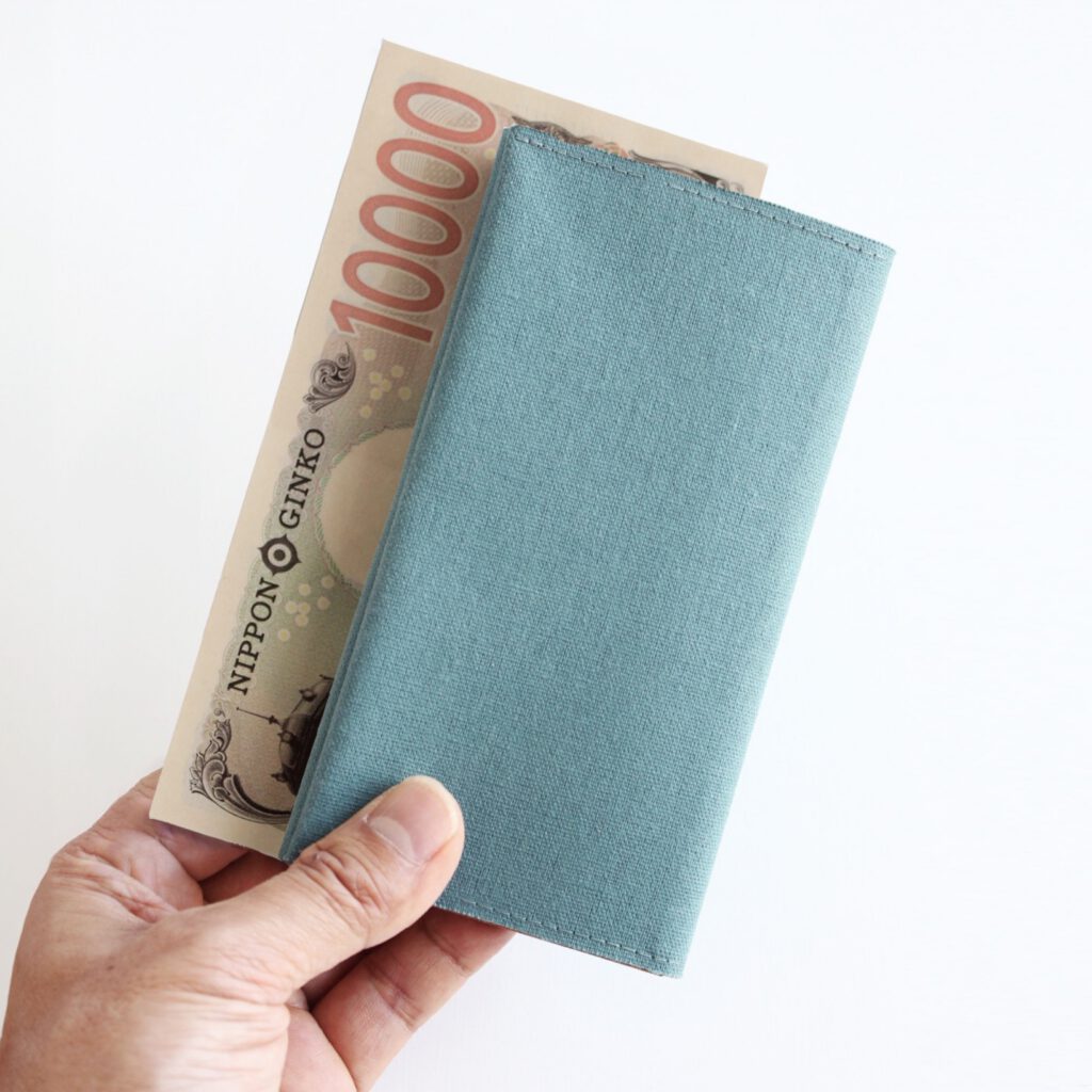 オーシャングリーン色の長財布と壱万円札も持っている手