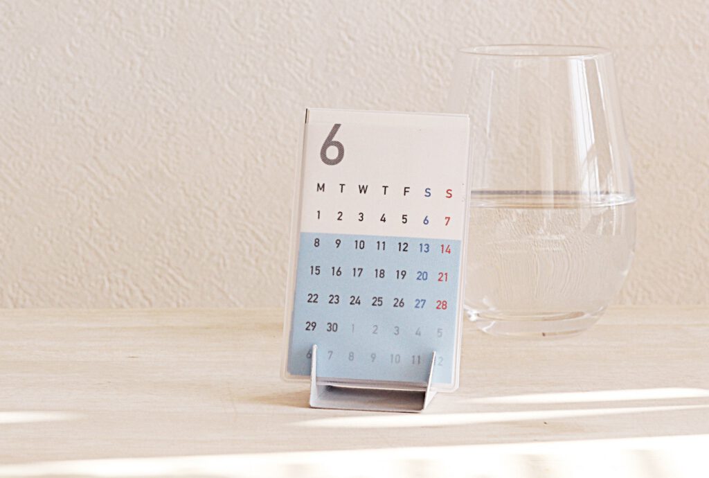 a cup full of calendar 名刺サイズカレンダーがスタンドに立てられている、横には水の入ったグラスがある。