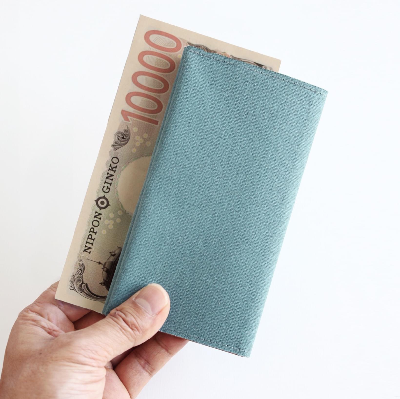 オーシャングリーン色の長財布と壱万円札も持っている手